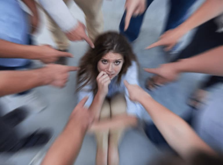 Un cerchio di braccia punta il dito indice verso una donna impaurita